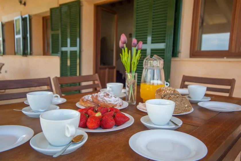 Una mesa de desayuno está servida con tazas, pasteles, fresas y jugo de naranja.