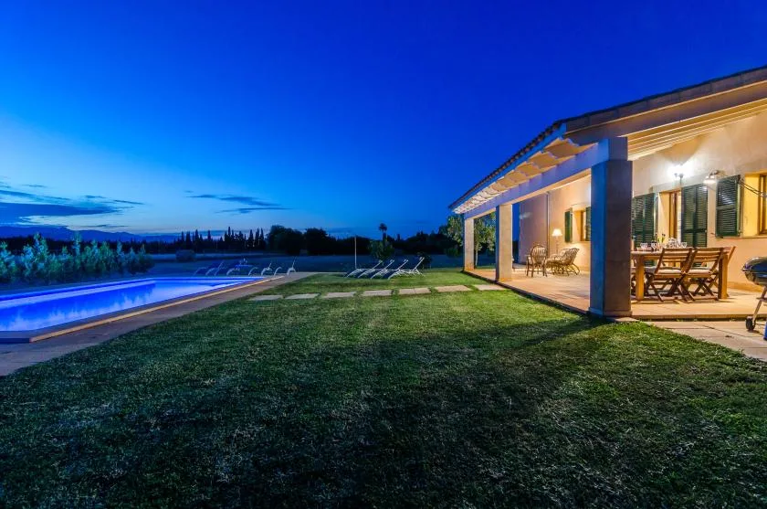 Un patio y una piscina junto a una casa iluminada al atardecer.