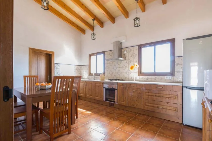 Cocina y comedor con armarios de madera, una mesa y vigas de techo a la vista.