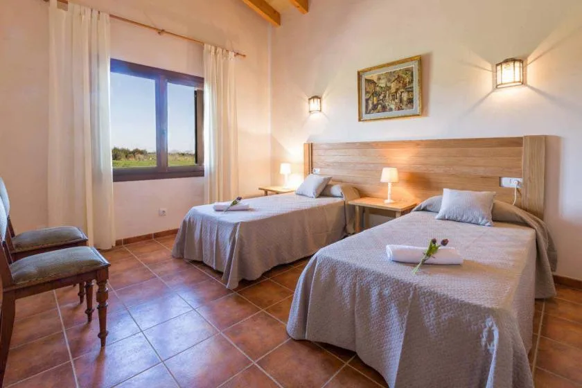 Un dormitorio con dos camas, un cabecero compartido y una ventana con cortinas.