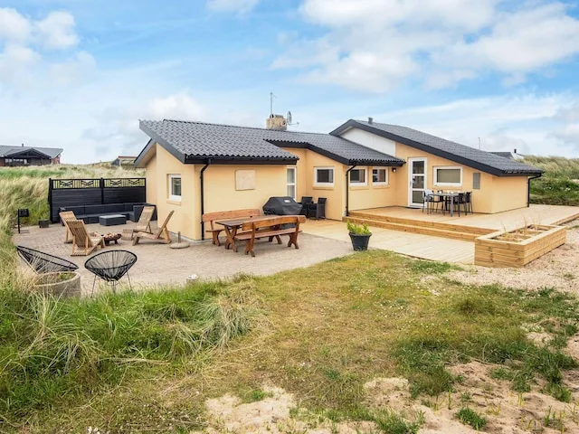 A yellow vacation house with outdoor seating and a deck in a sandy landscape.