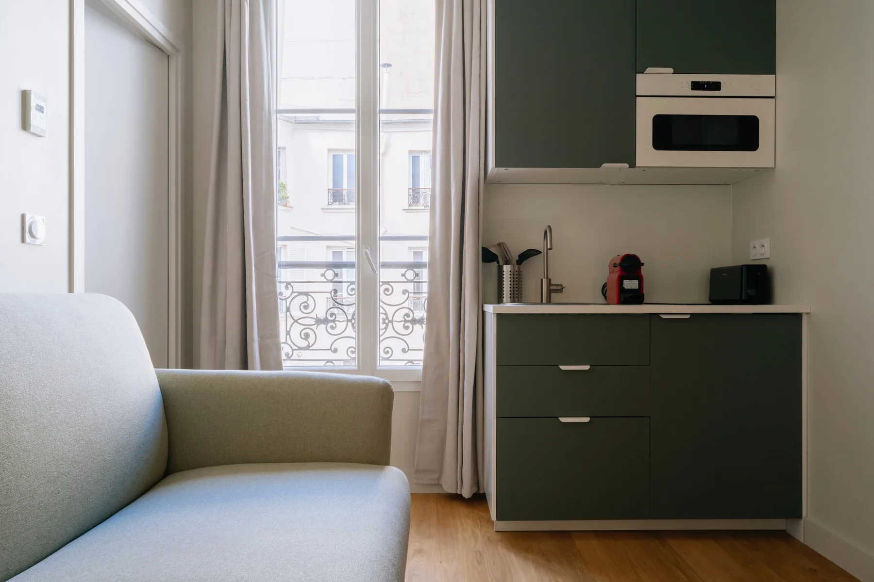 A compact living area with seating beside a kitchenette and tall window.