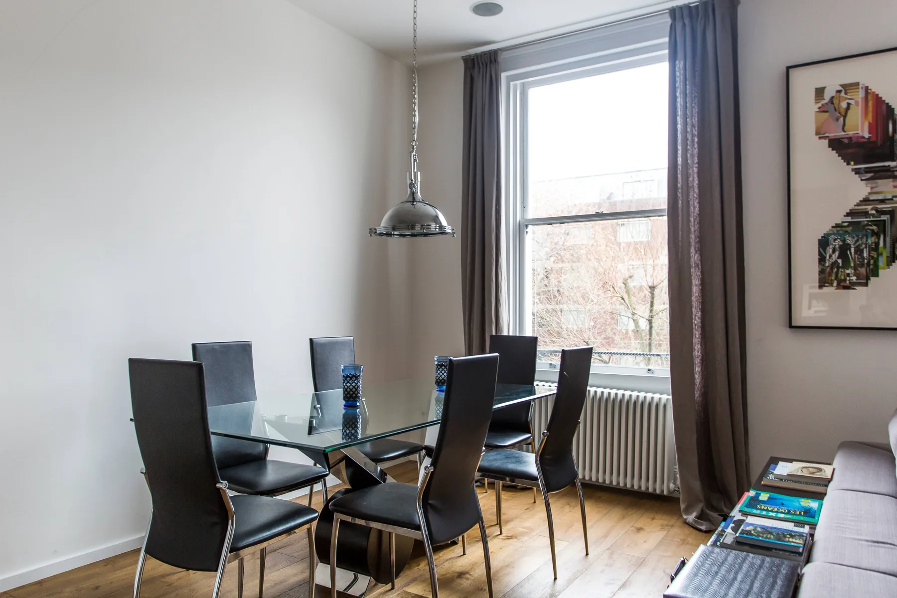 Un comedor con una mesa de vidrio y asientos oscuros junto a una ventana grande.