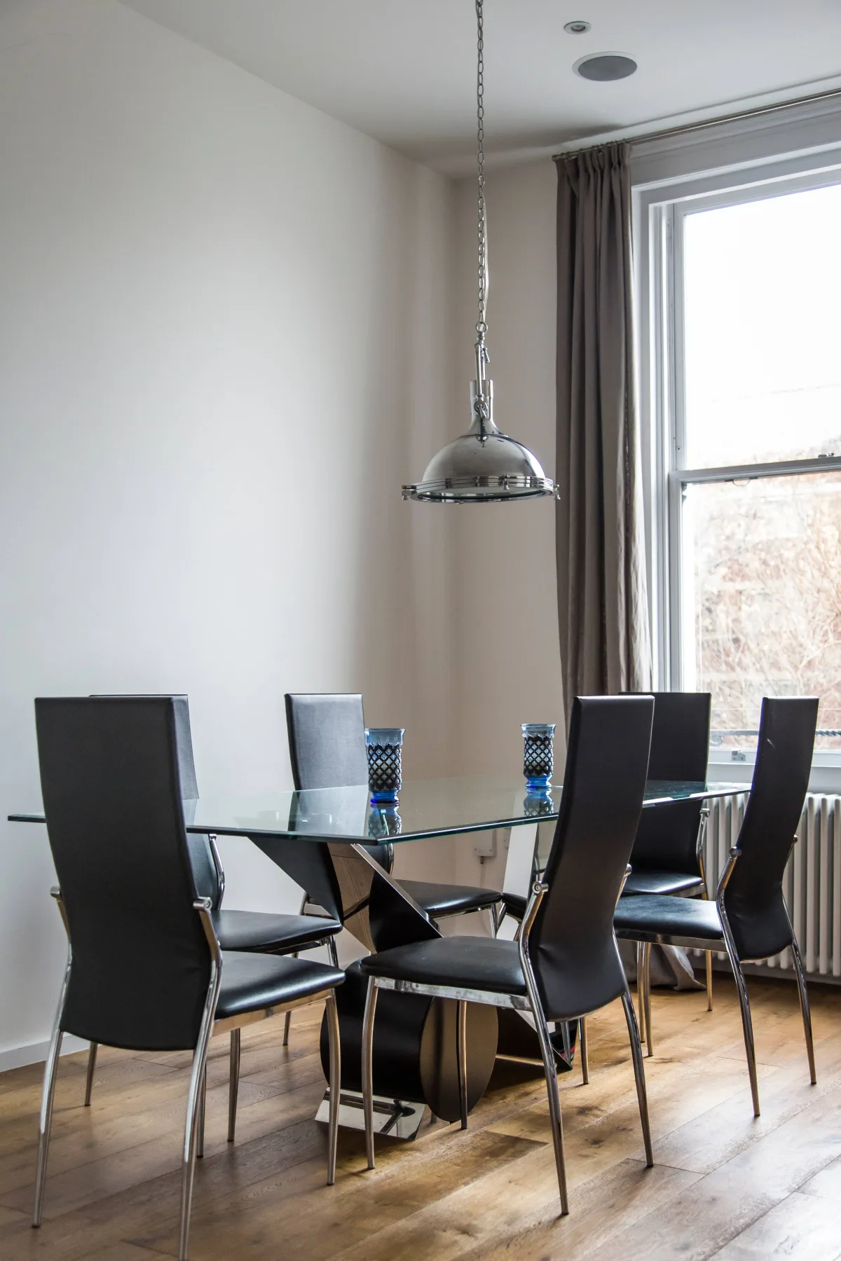 Comedor con mesa de vidrio y asientos oscuros junto a una ventana grande.