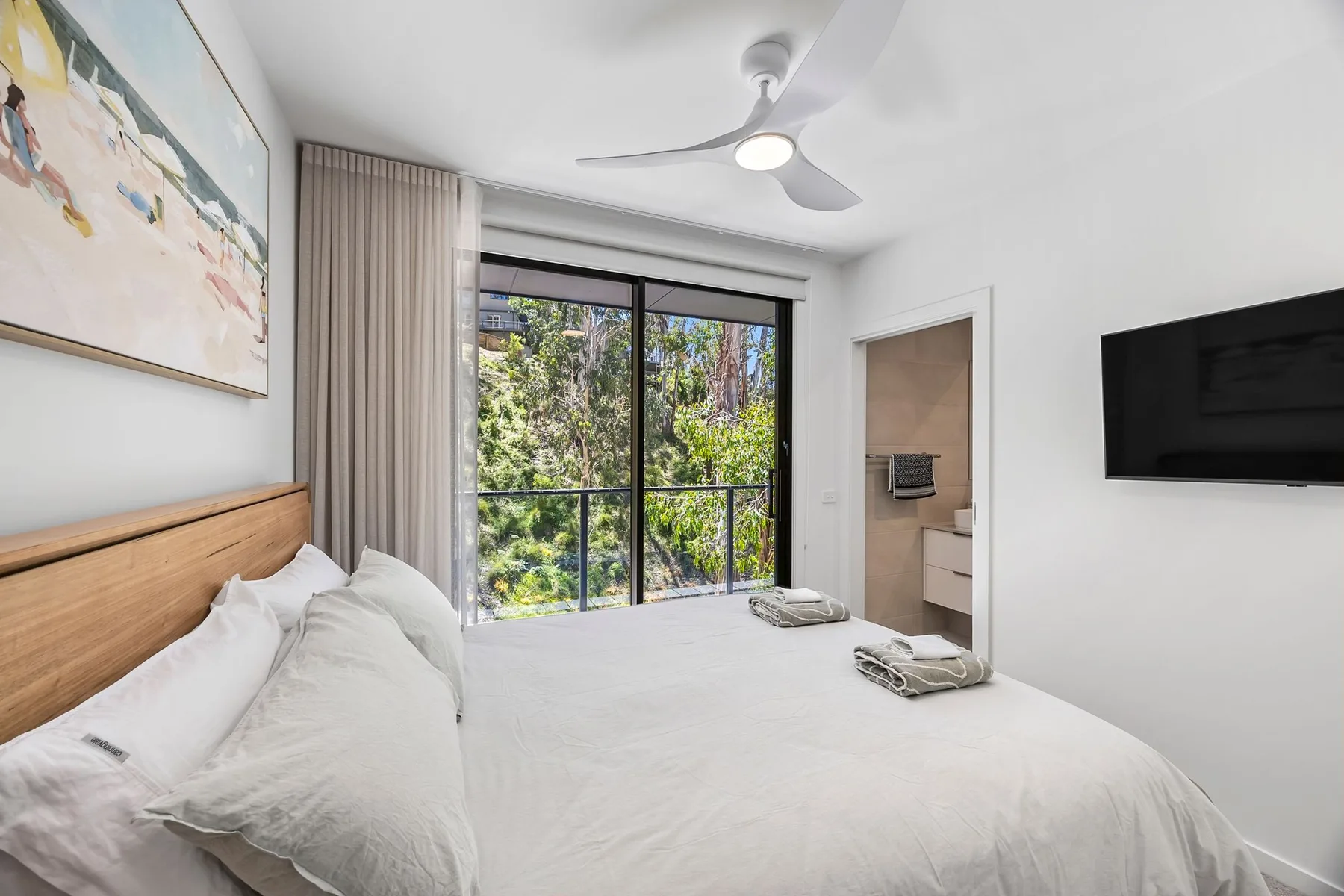 Un dormitorio luminoso con una cama grande, puertas corredizas de vidrio y vistas frondosas.