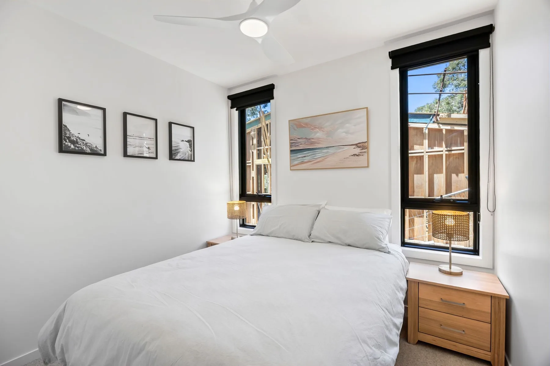 Un dormitorio luminoso con una cama tendida y cuadros en la pared.