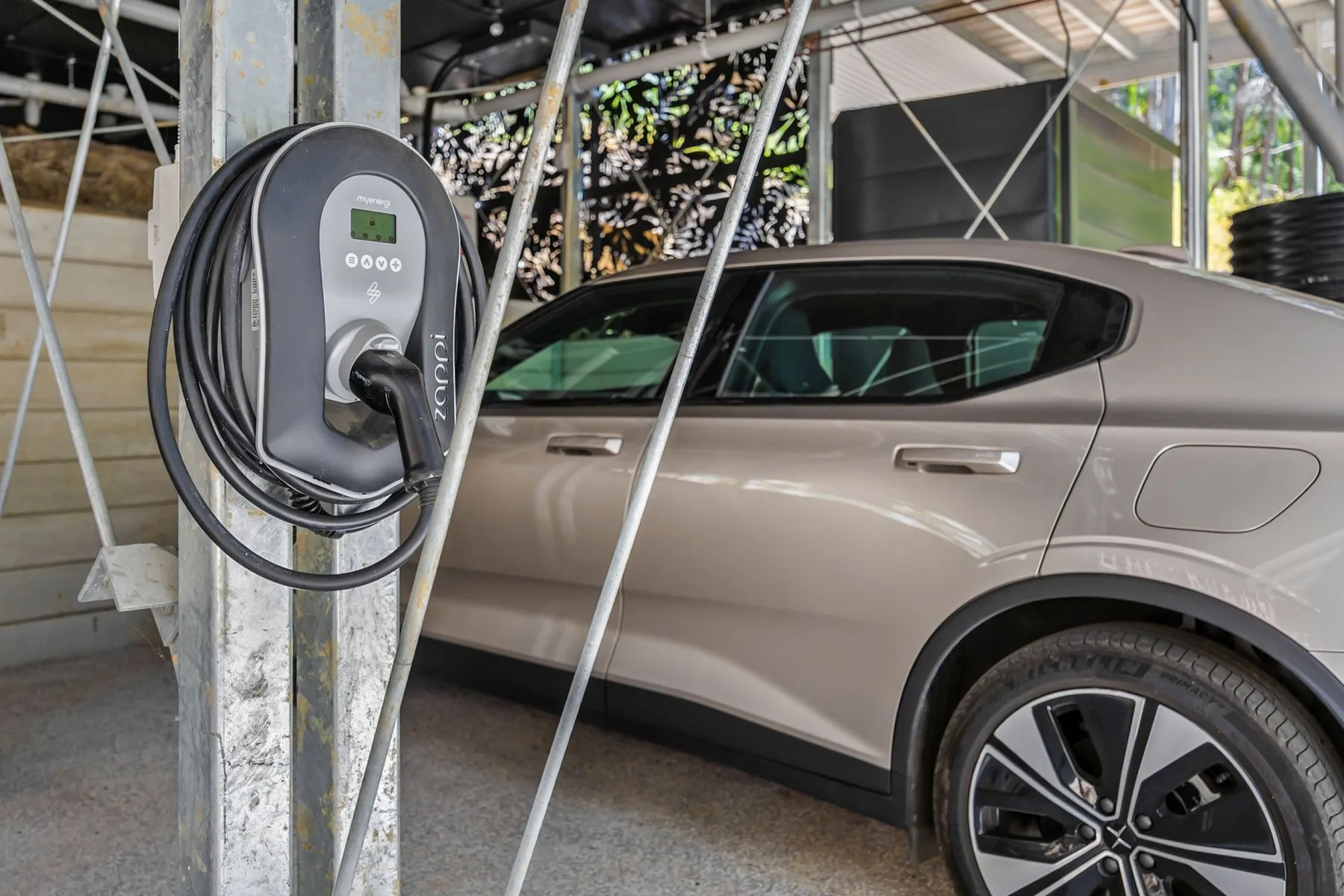 Un automóvil está junto a una estación de carga para vehículos eléctricos bajo una estructura techada.