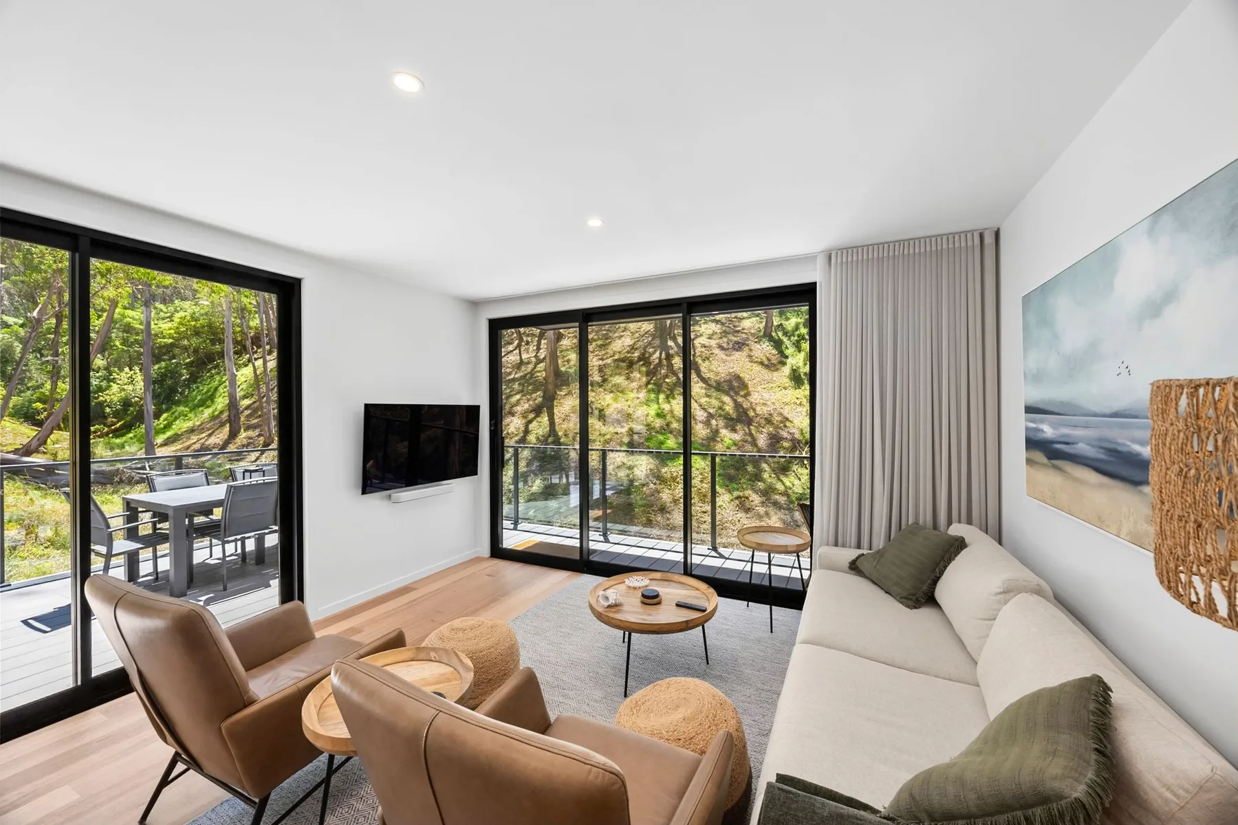 Una sala luminosa con asientos, un televisor en la pared y grandes ventanas con vista a los árboles.