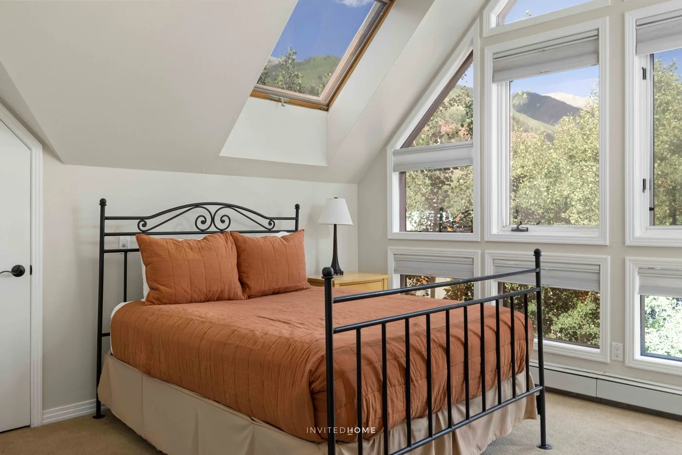 Dormitorio con una cama junto a grandes ventanas con vistas a una ladera verde.
