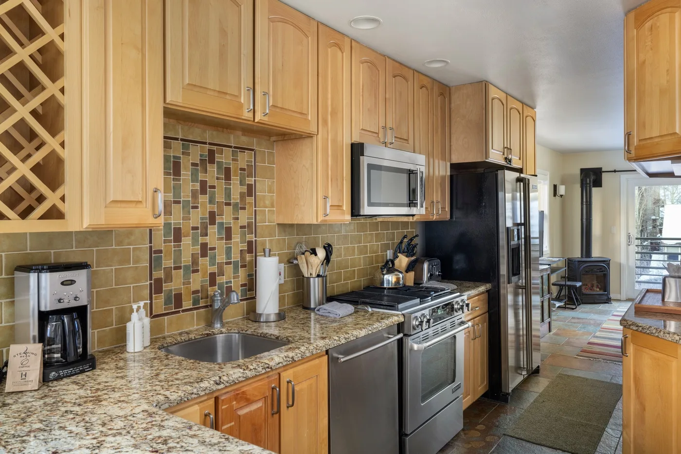 Una cocina con gabinetes de madera, un salpicadero de azulejos y electrodomésticos de acero inoxidable.
