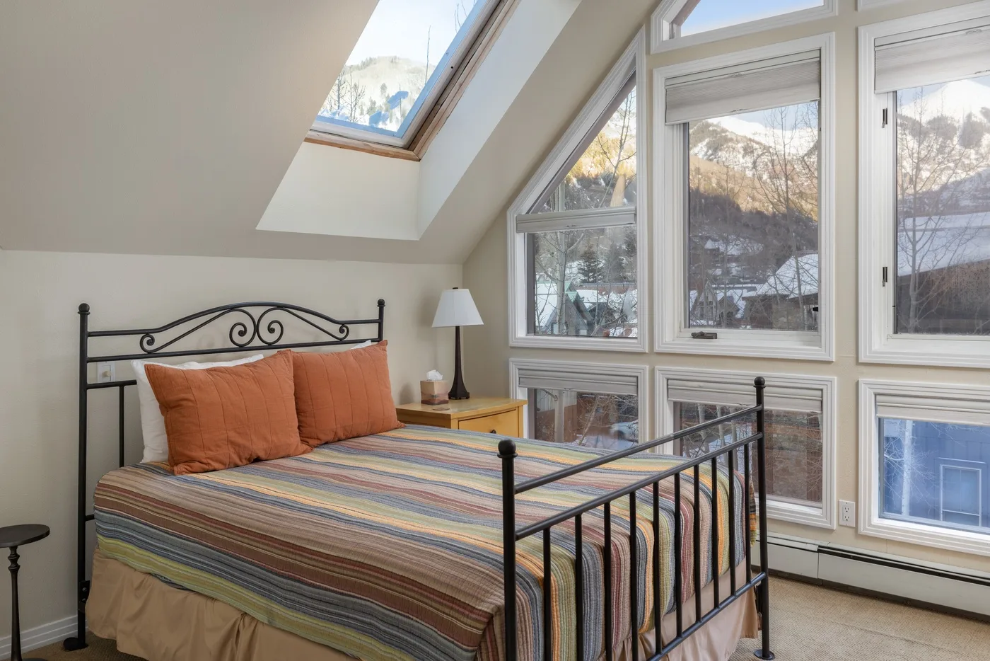 Un dormitorio con una cama de metal bajo techos inclinados y grandes ventanas.