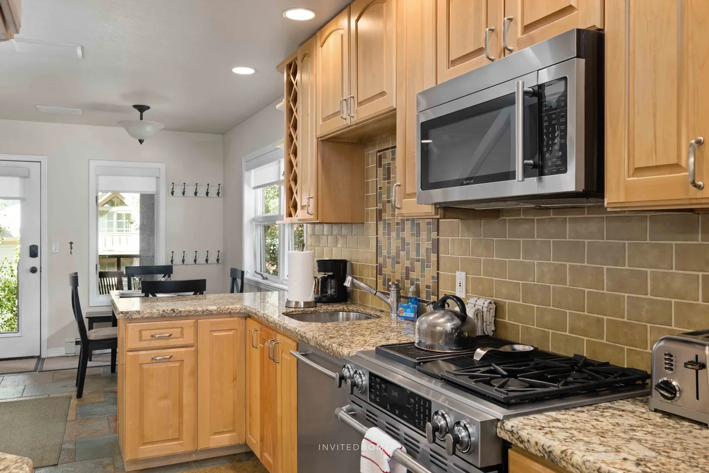 Una cocina luminosa con gabinetes de madera, salpicadero de azulejos y estufa de gas.