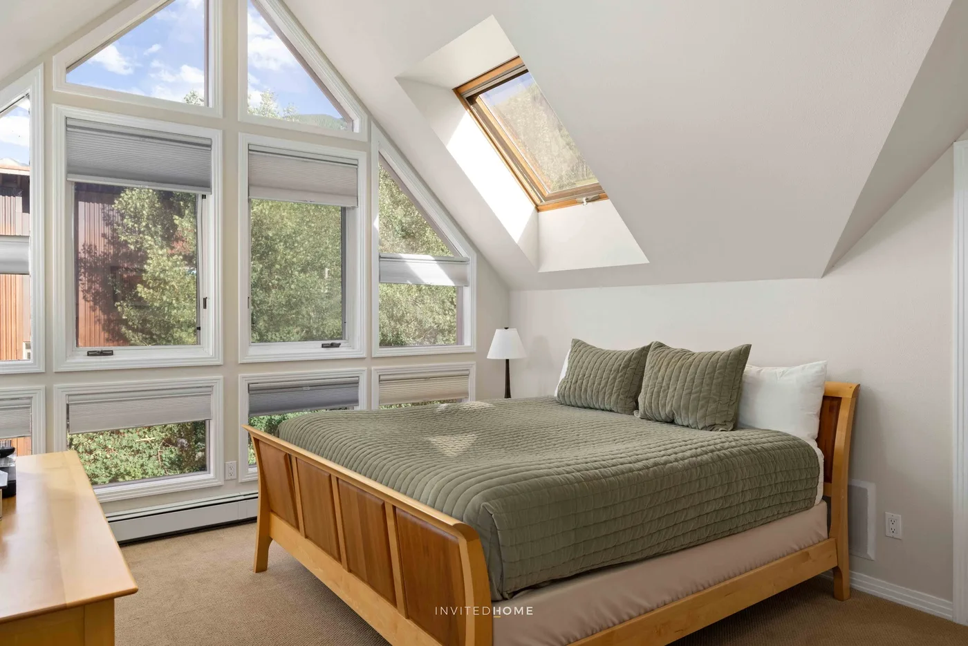 Dormitorio con una cama de madera y grandes ventanas bajo un techo inclinado.