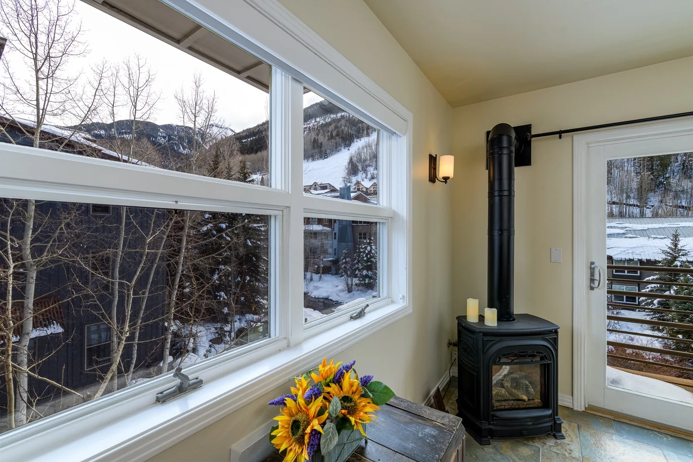 Una habitación luminosa con grandes ventanas hacia un paisaje nevado y una estufa de leña.