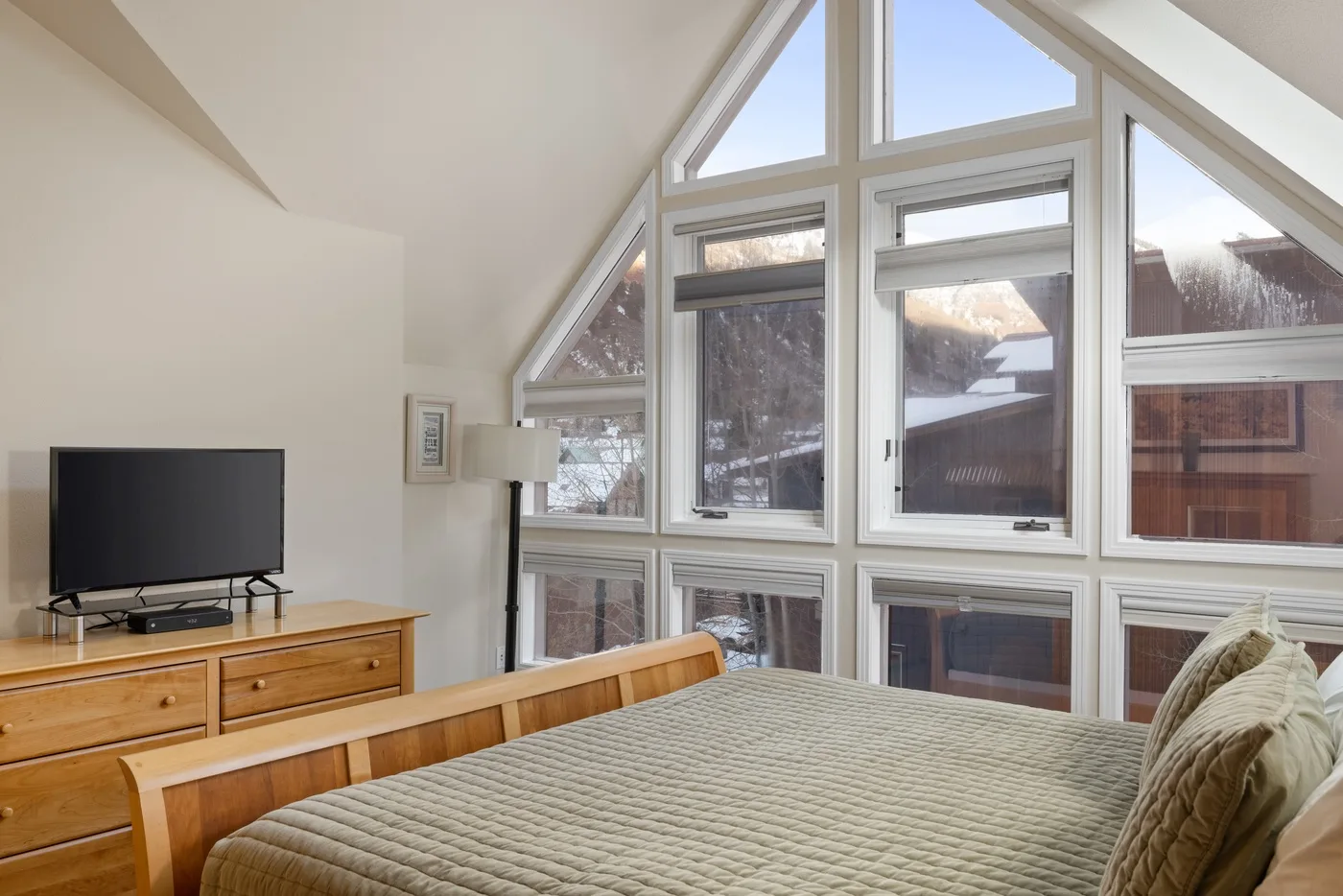 Un dormitorio con una cama junto a grandes ventanas y un televisor.