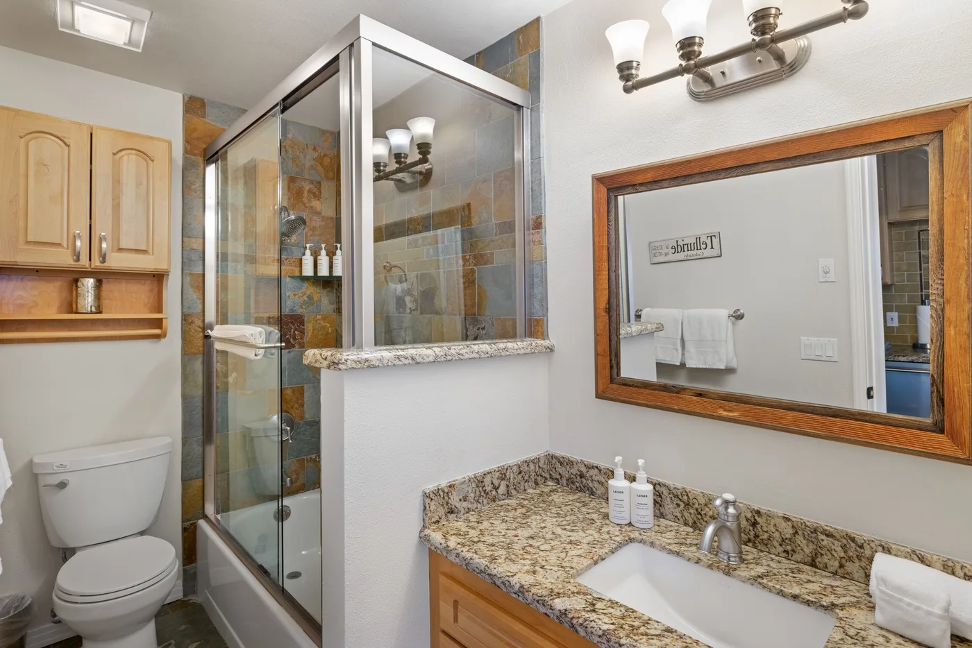 Baño con ducha de vidrio, lavabo y gabinetes de madera.
