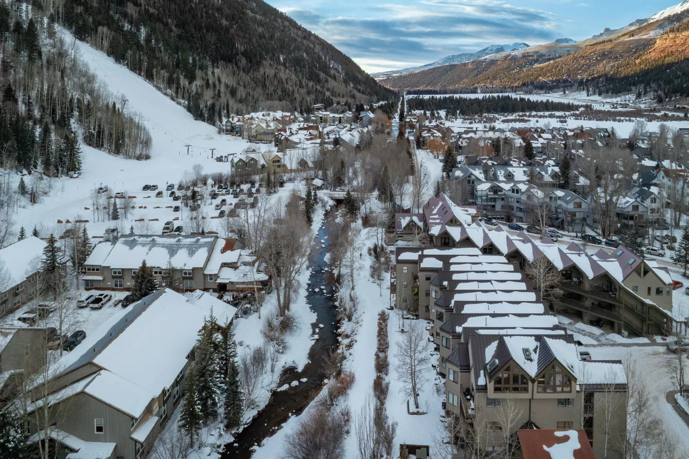 Un pueblo de montaña cubierto de nieve, con edificios junto a un arroyo sinuoso.