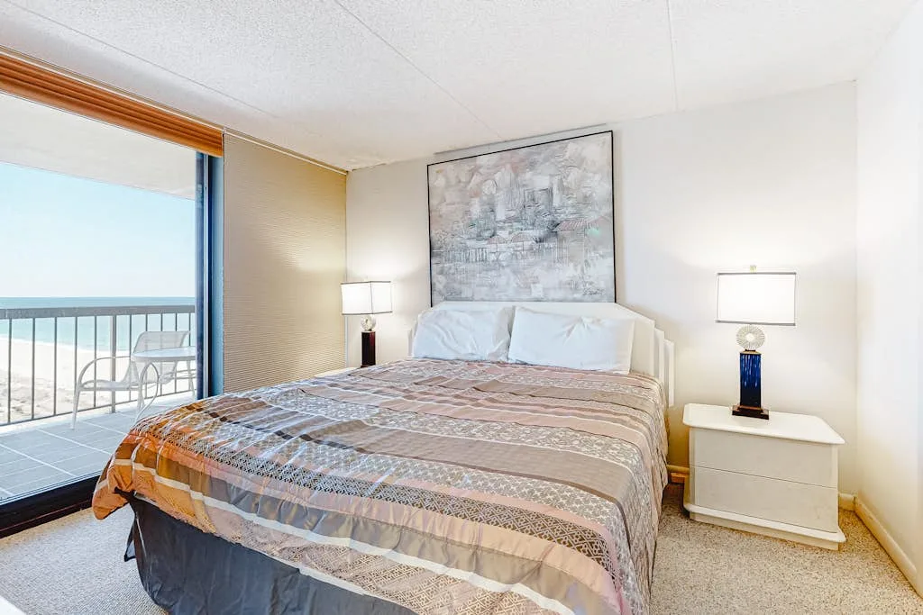 A bedroom with a made bed, bedside lamps, and a sliding glass door to a balcony.