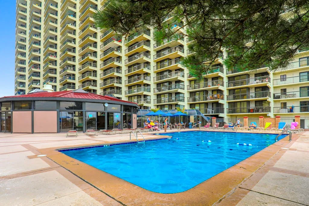 An outdoor swimming pool beside a high-rise building, with lounge chairs along the deck.