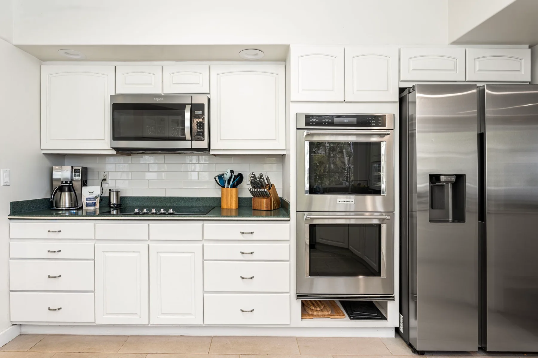 Una cocina luminosa con gabinetes blancos, electrodomésticos de acero inoxidable y una encimera oscura.