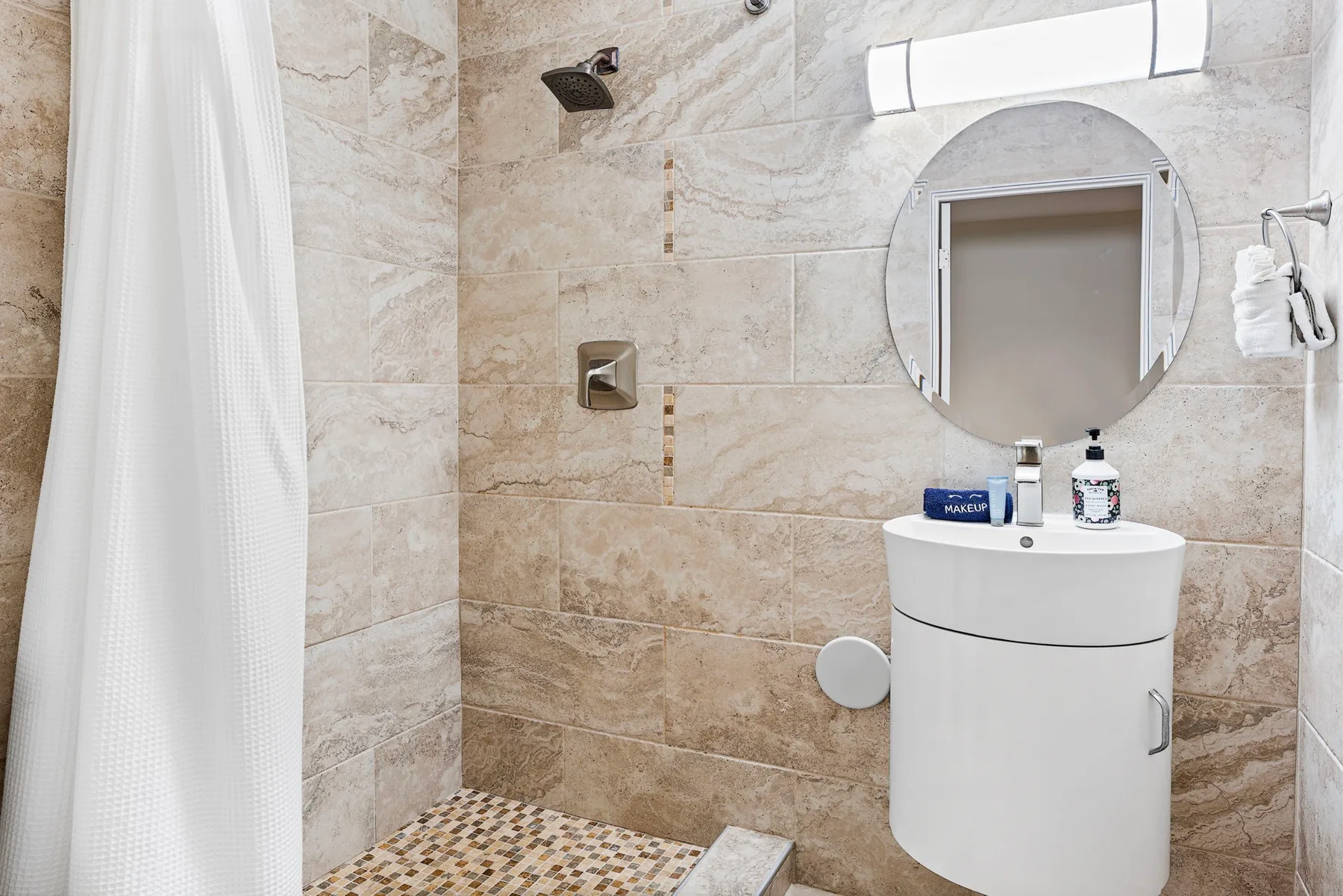 Un baño alicatado con ducha, lavabo y espejo redondo.