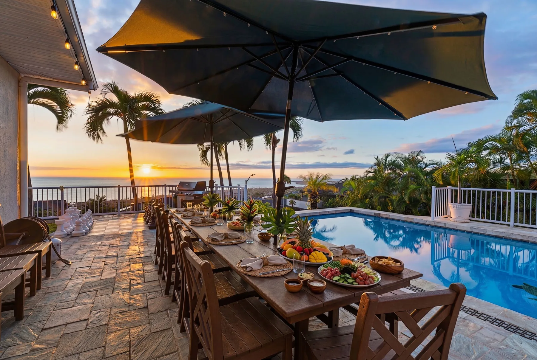 Un patio comedor junto a la piscina mira al océano al atardecer, con una larga mesa al aire libre.