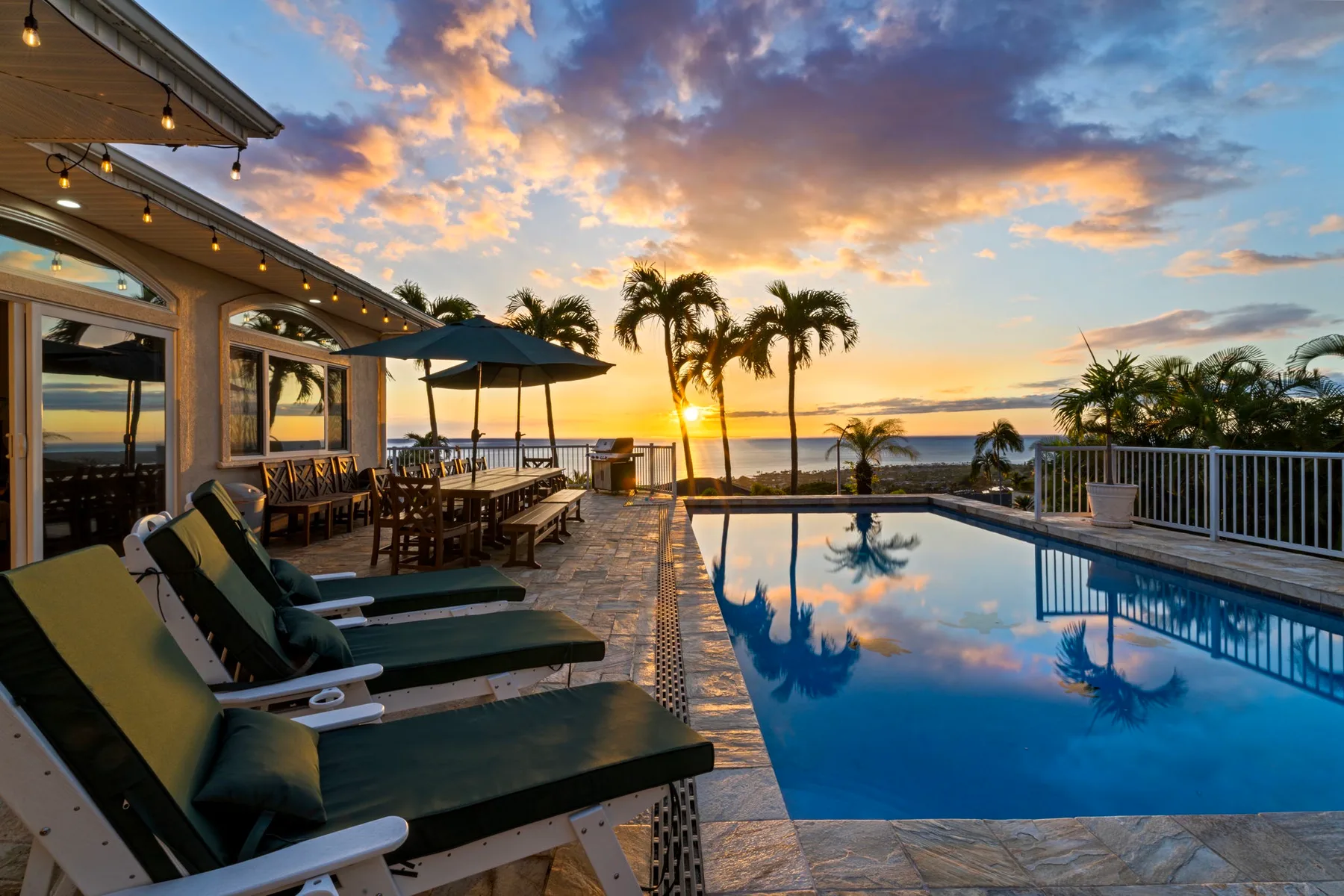 Un patio junto a la piscina con asientos reclinables mira al mar al atardecer.