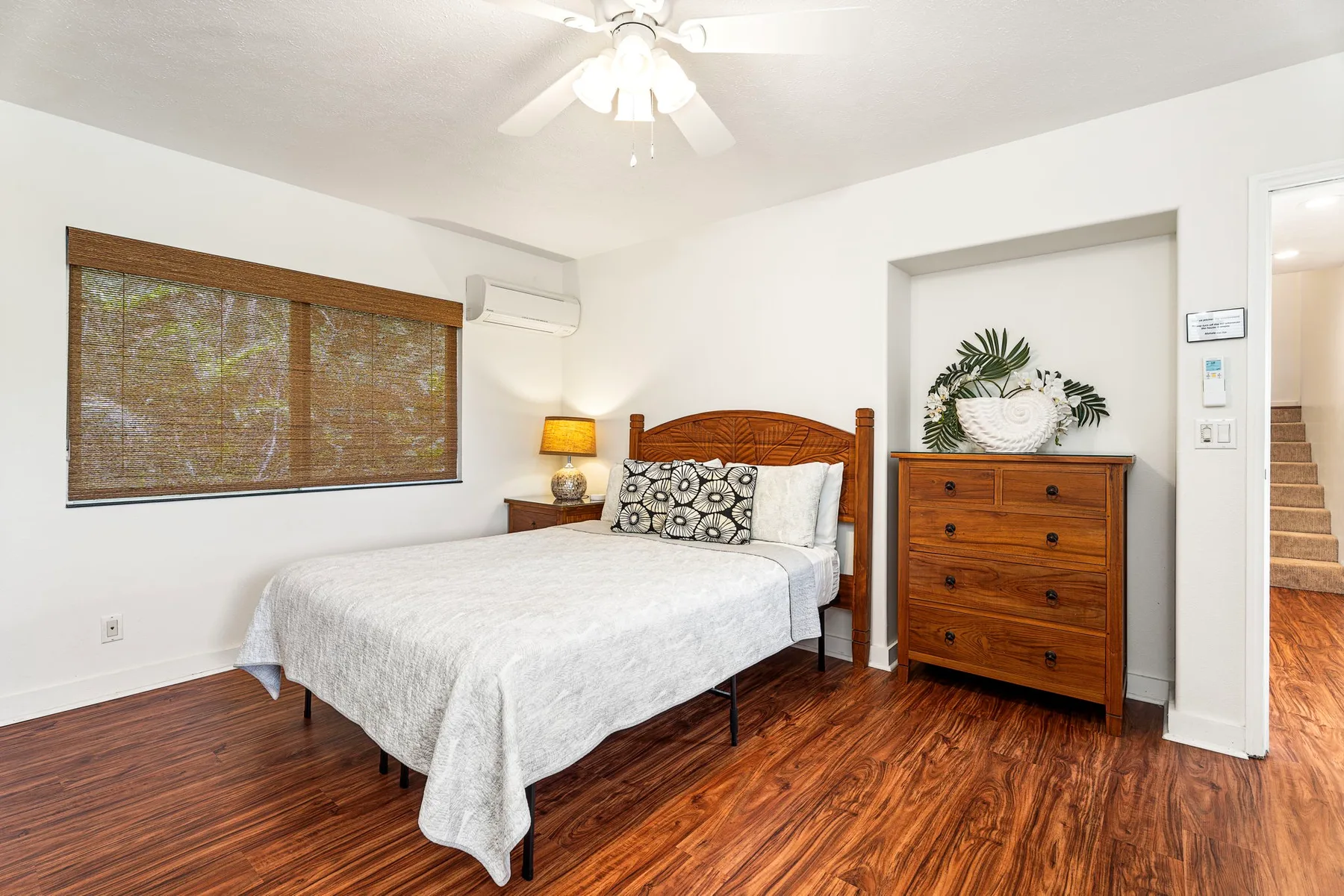 Un dormitorio con una cama, una cómoda y una ventana con persiana tejida.
