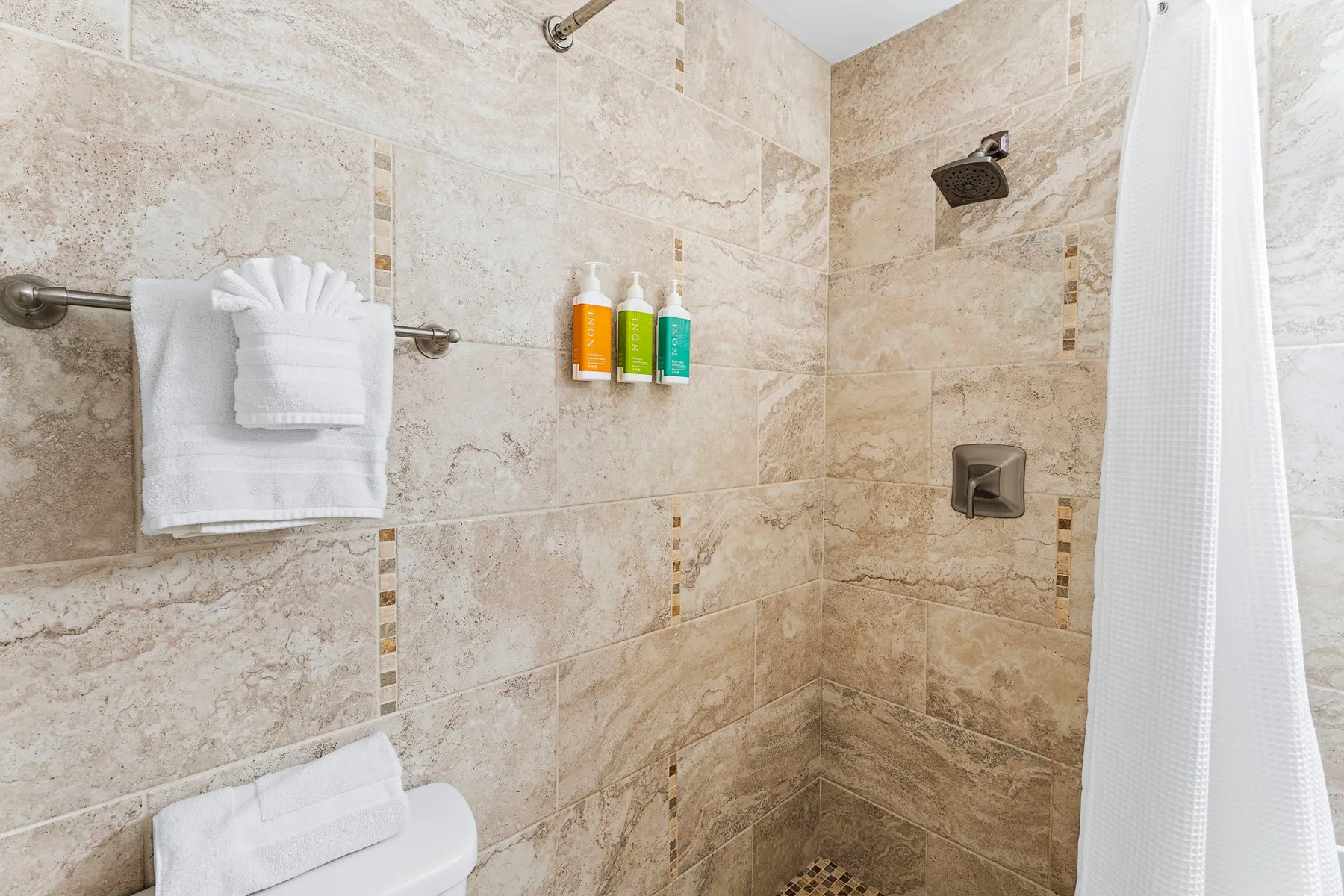 Una ducha de baño con azulejos, cortina y toallas blancas dobladas.