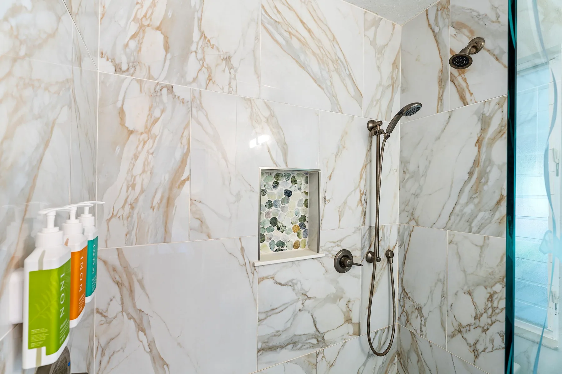 Una zona de ducha revestida de azulejos, con accesorios de pared y un pequeño nicho.