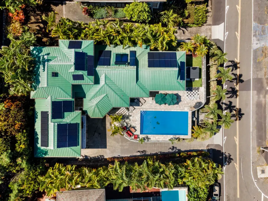 Vista aérea de una propiedad con techos verdes, una piscina y vegetación tropical alrededor.