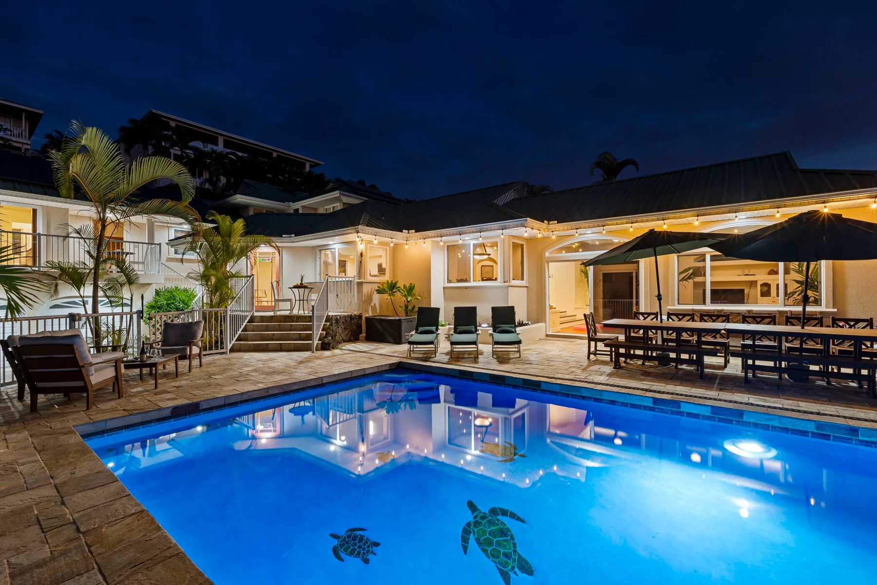 Una piscina iluminada junto a un patio y comedor al aire libre por la noche.