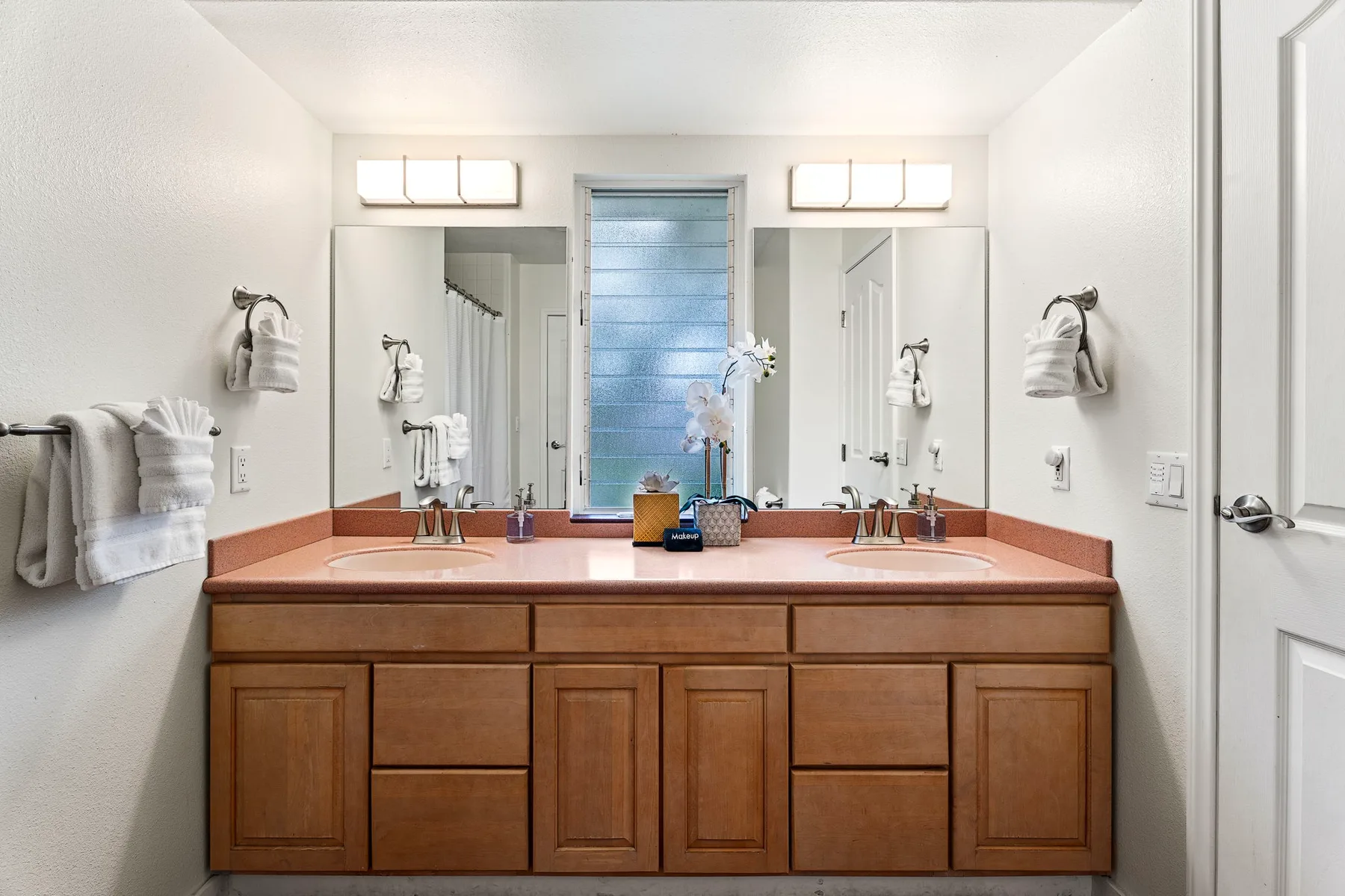 Un tocador de baño con dos lavabos y espejos bajo luces brillantes.