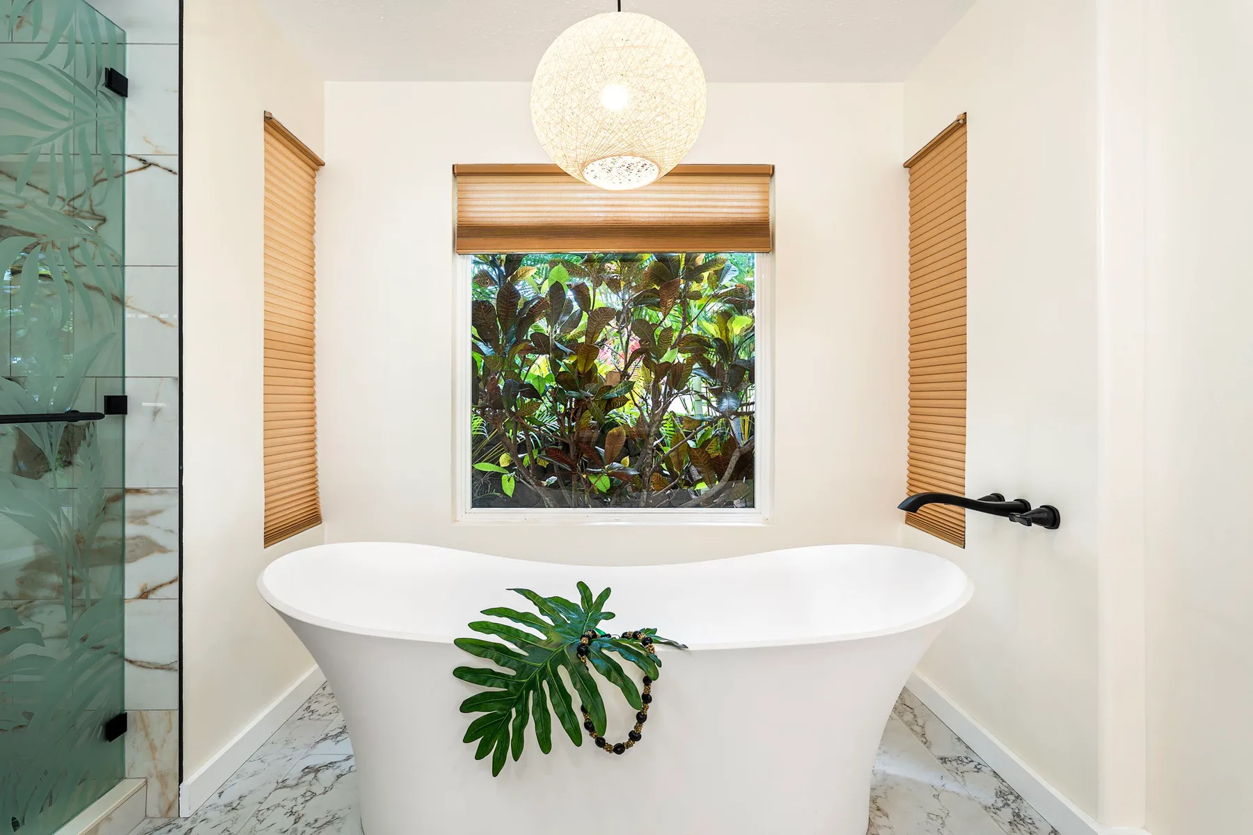Un baño cuenta con una bañera exenta bajo una ventana con vegetación frondosa.