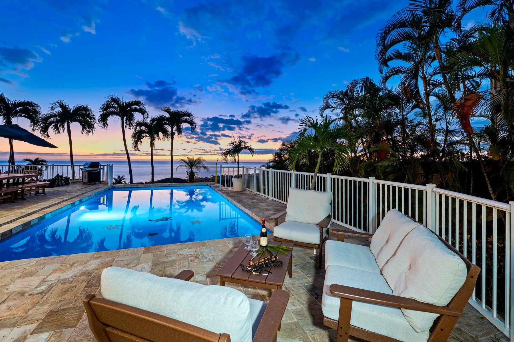 Un patio con piscina y asientos acolchados da al agua al atardecer.