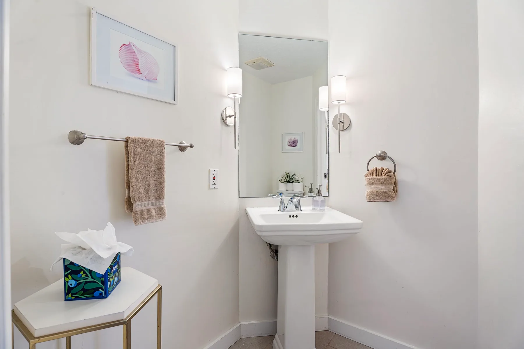 Un baño luminoso con lavabo de pedestal, espejo de pared y toallas de mano.