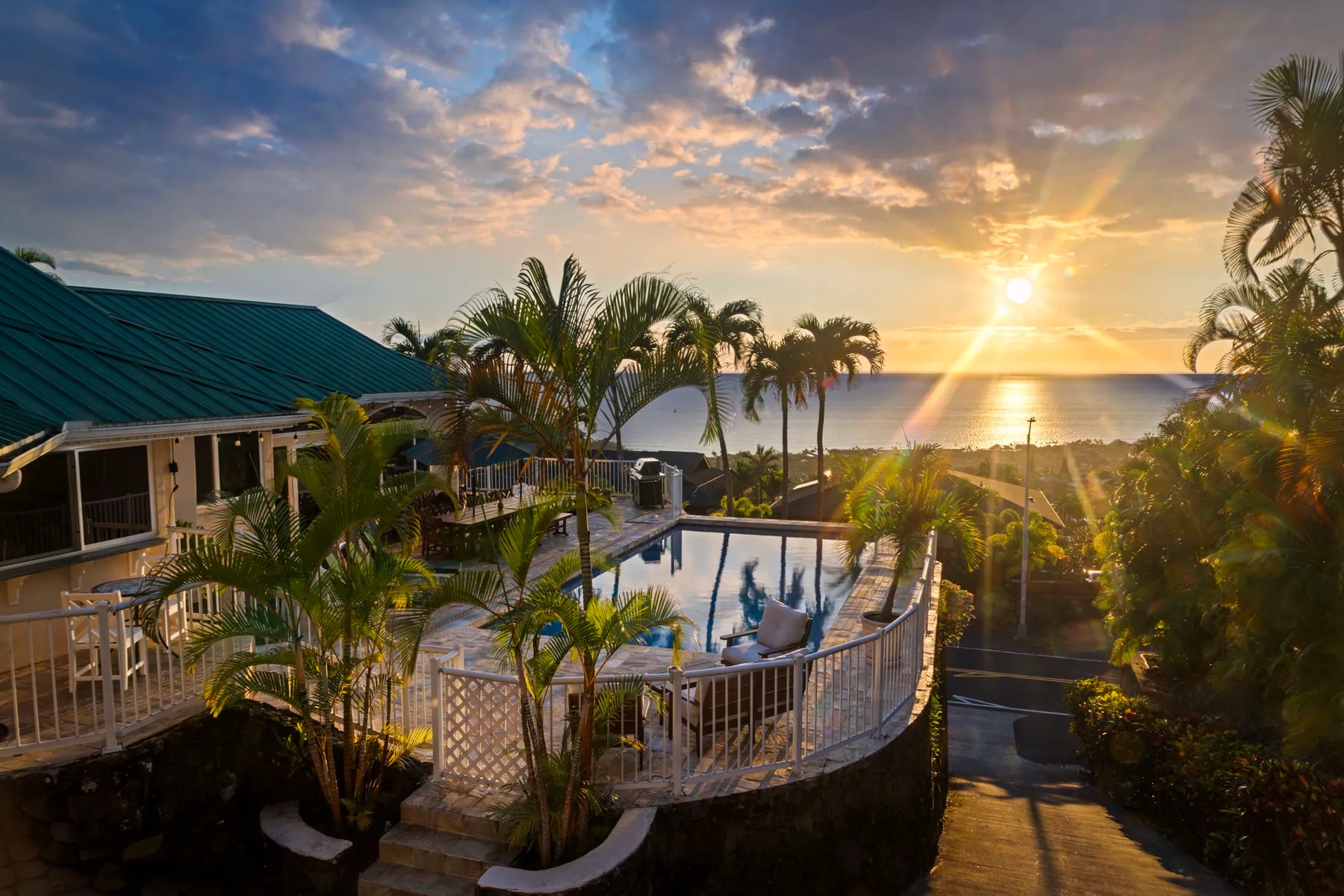 Una piscina tropical al aire libre mira al océano al atardecer, rodeada de palmeras.