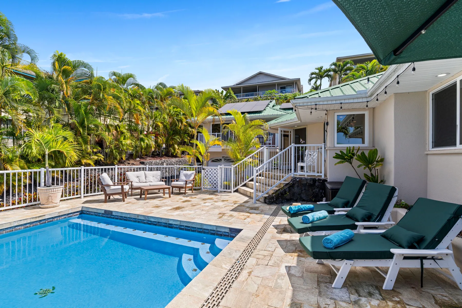 Una piscina al aire libre junto a un patio con asientos y plantas tropicales.