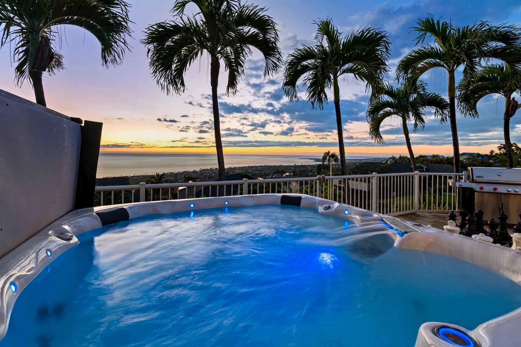 Una piscina iluminada mira hacia el agua bajo palmeras al atardecer.