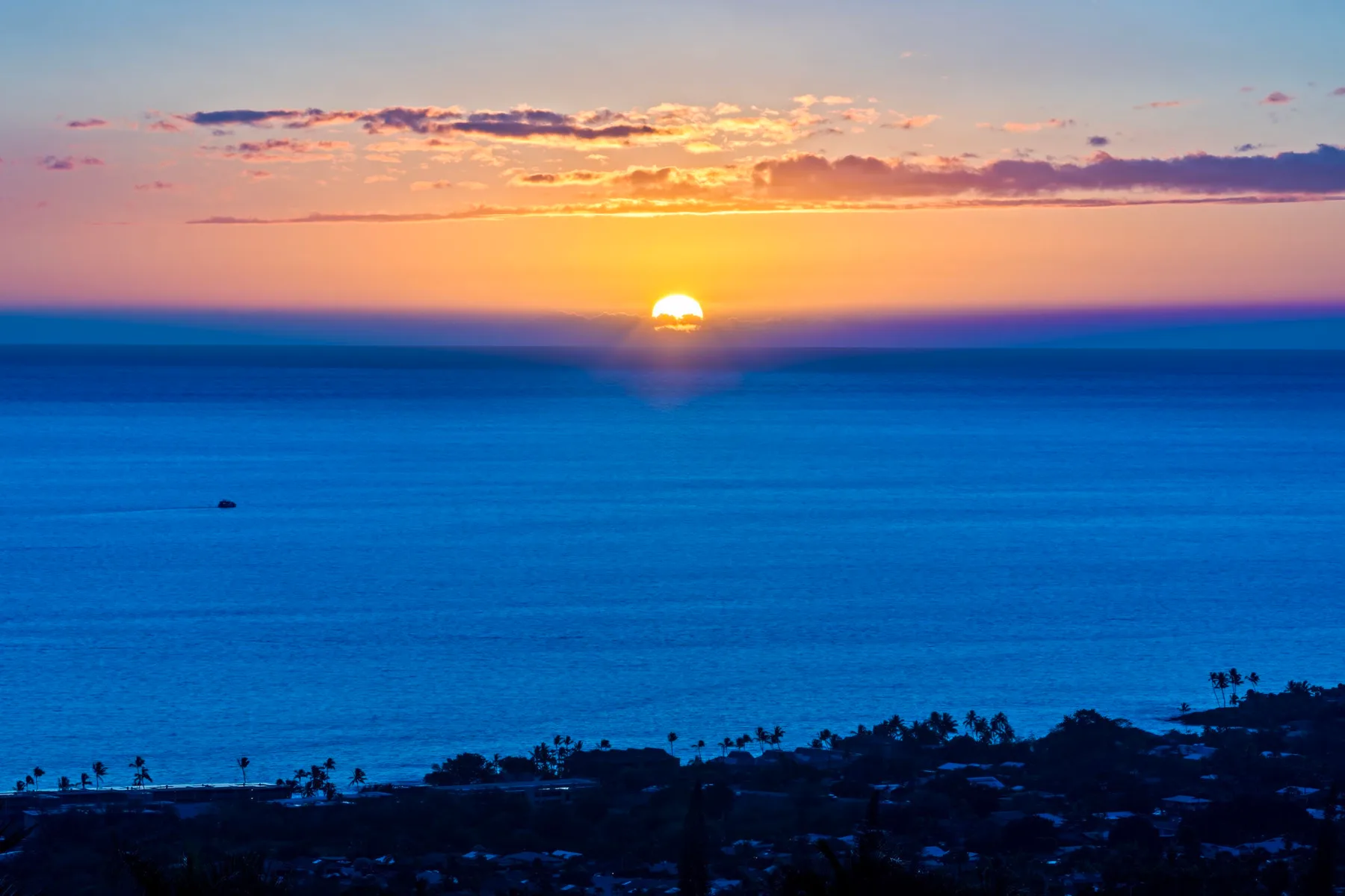 Atardecer sobre el océano, con una costa oscura en primer plano.