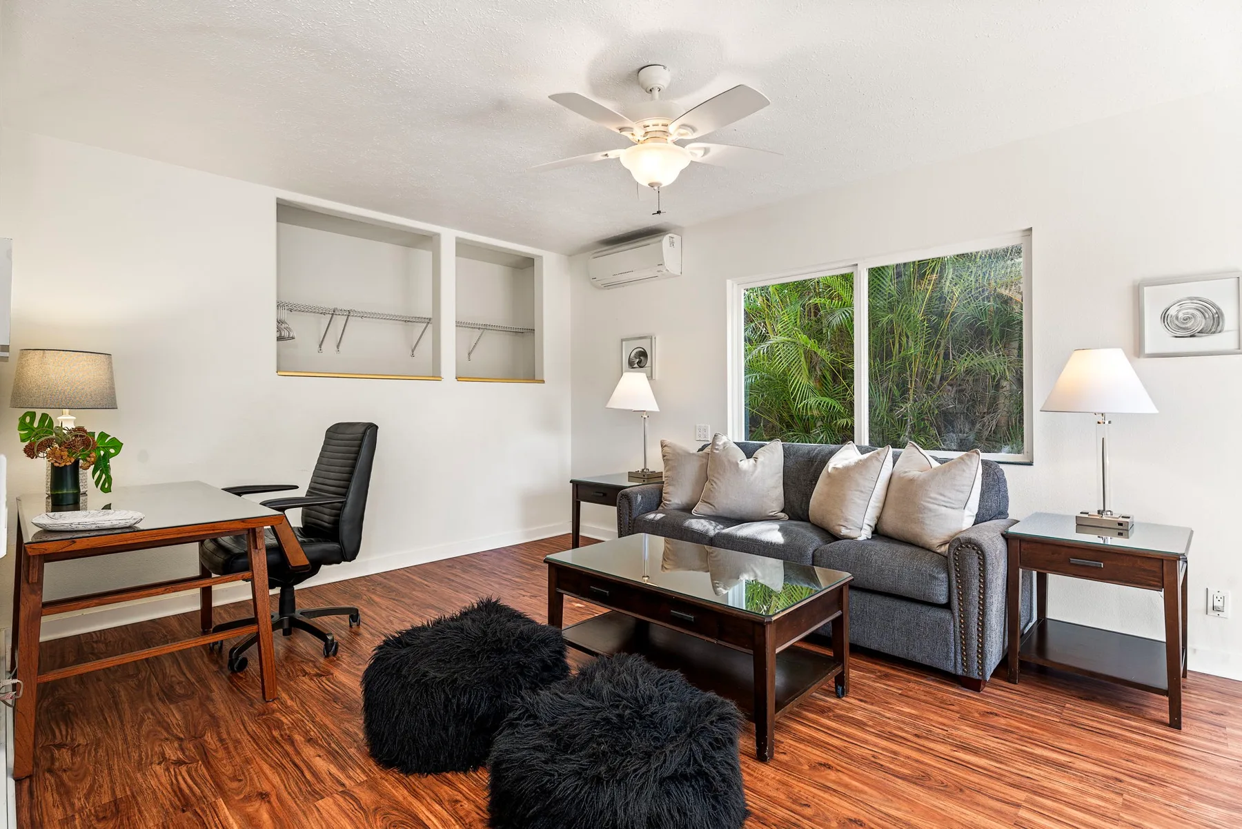 Una sala de estar con sofá, mesa de centro y escritorio junto a grandes ventanas.