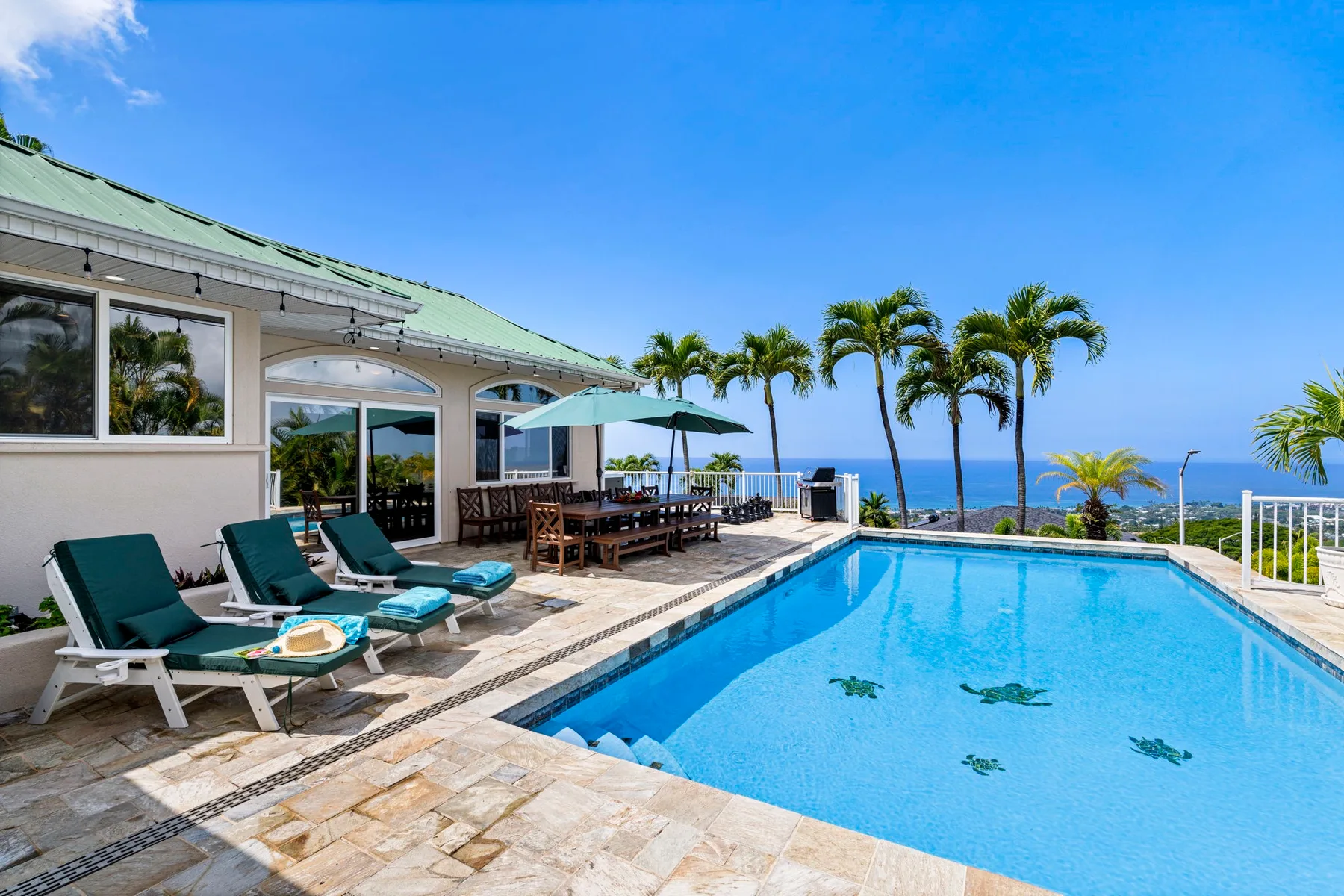 Una piscina al aire libre junto a un patio con asientos y palmeras.