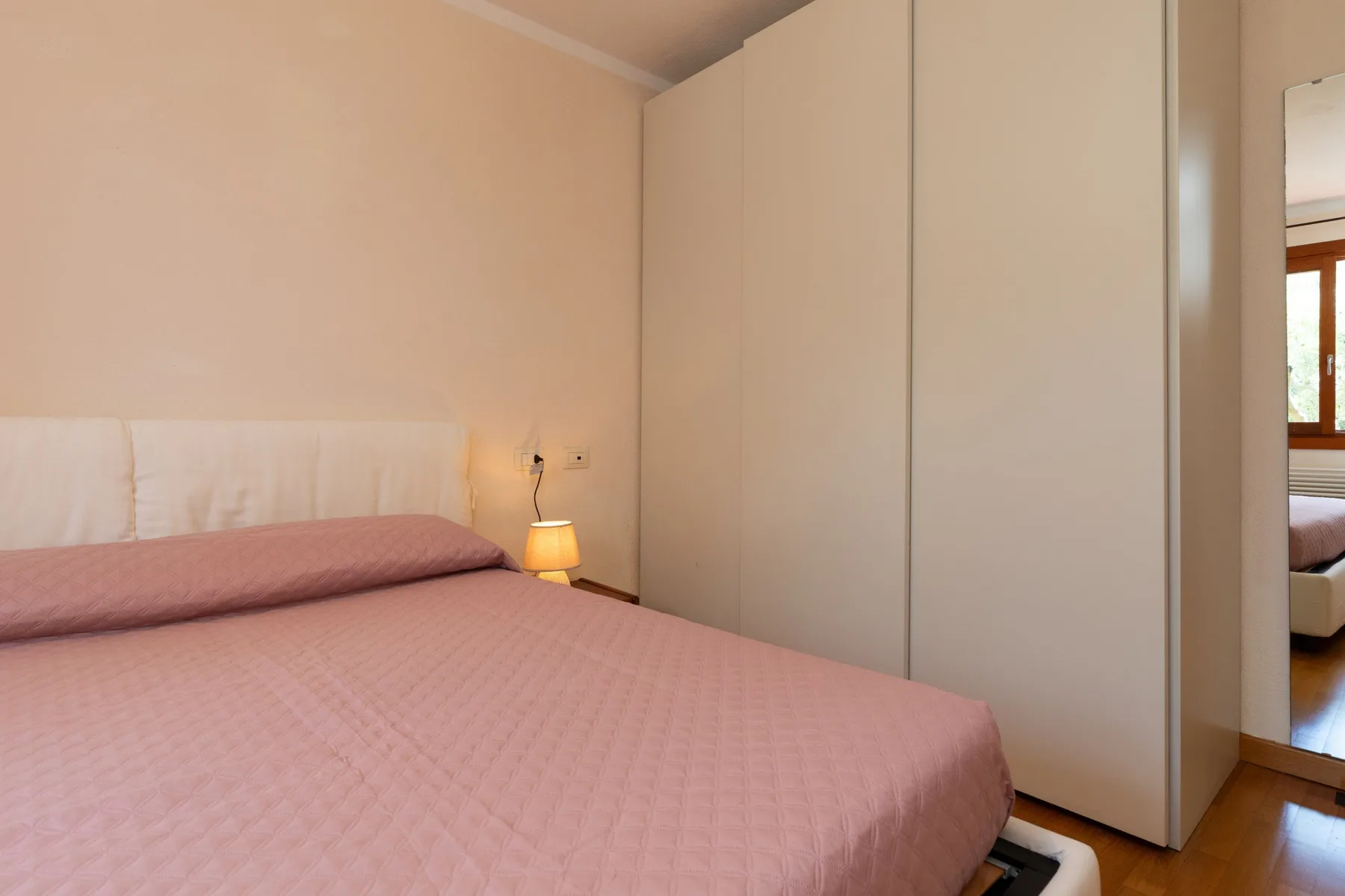 Un dormitorio con una cama cubierta de rosa y un armario alto.