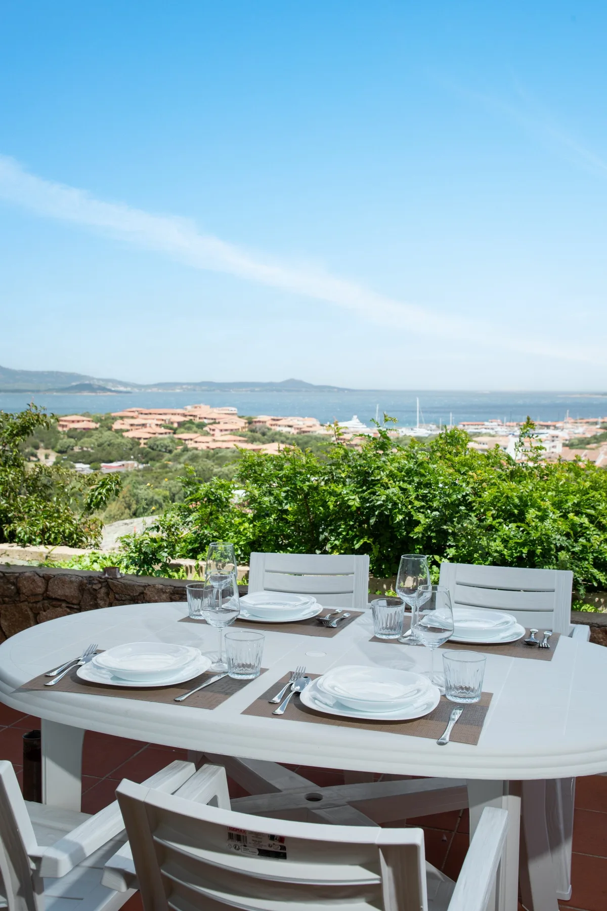 Una zona de comedor al aire libre ofrece vistas a la vegetación, edificios costeros y el mar.