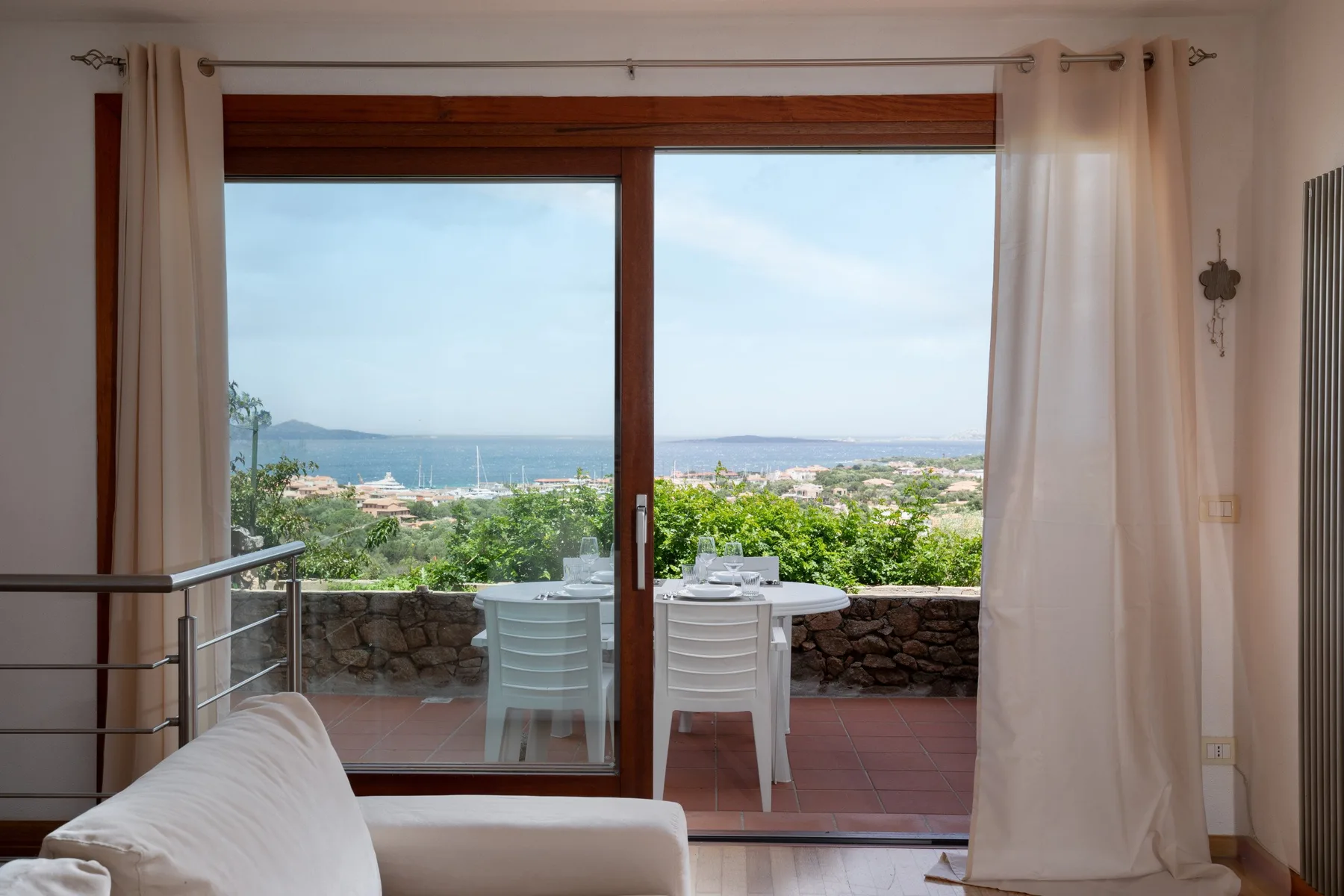 Una habitación luminosa da a una terraza con vegetación y vistas al mar.