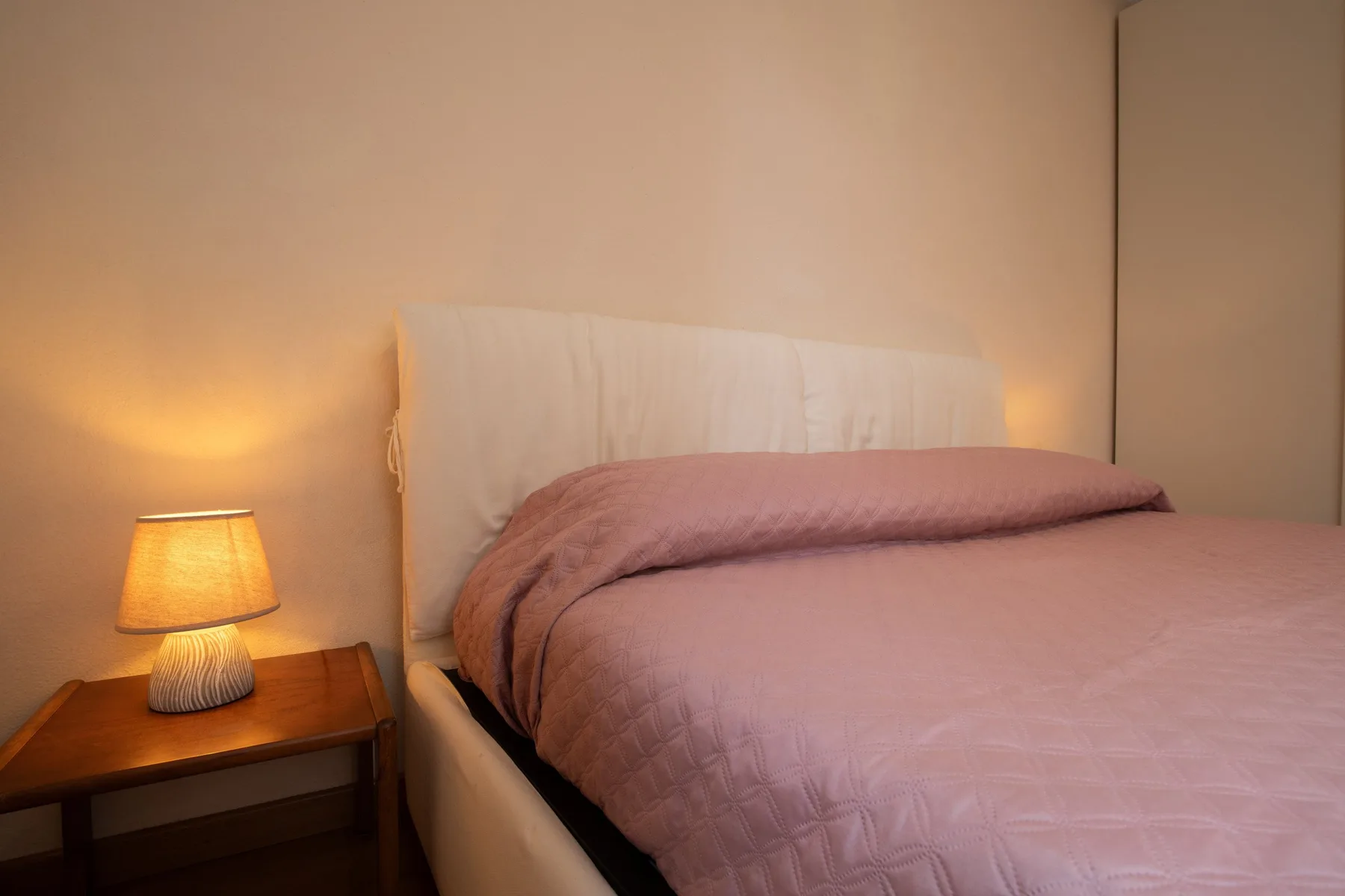 Un dormitorio con una cama vestida con ropa de cama rosa y una lámpara encendida.
