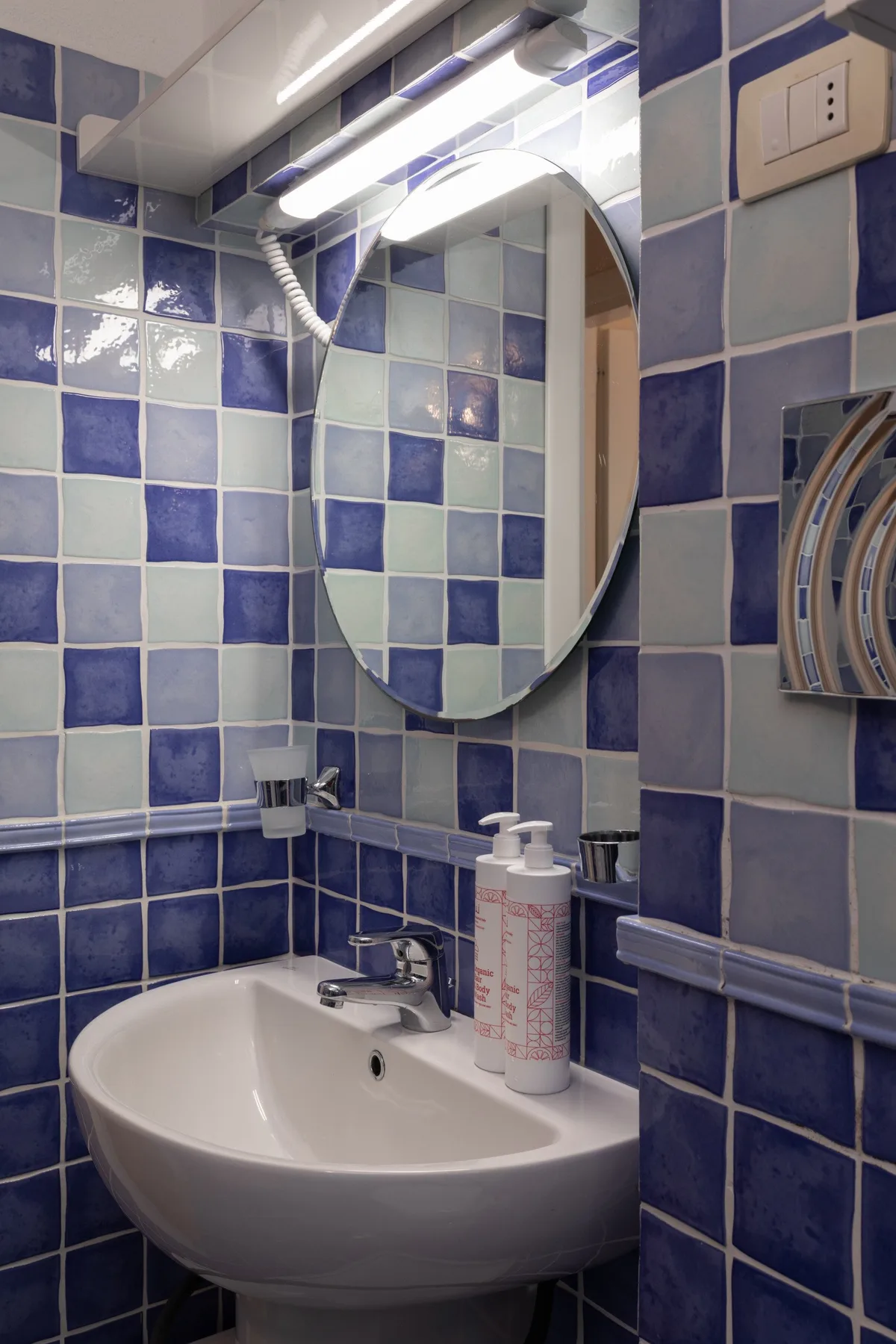 Un baño con azulejos, lavabo, espejo y luz superior.