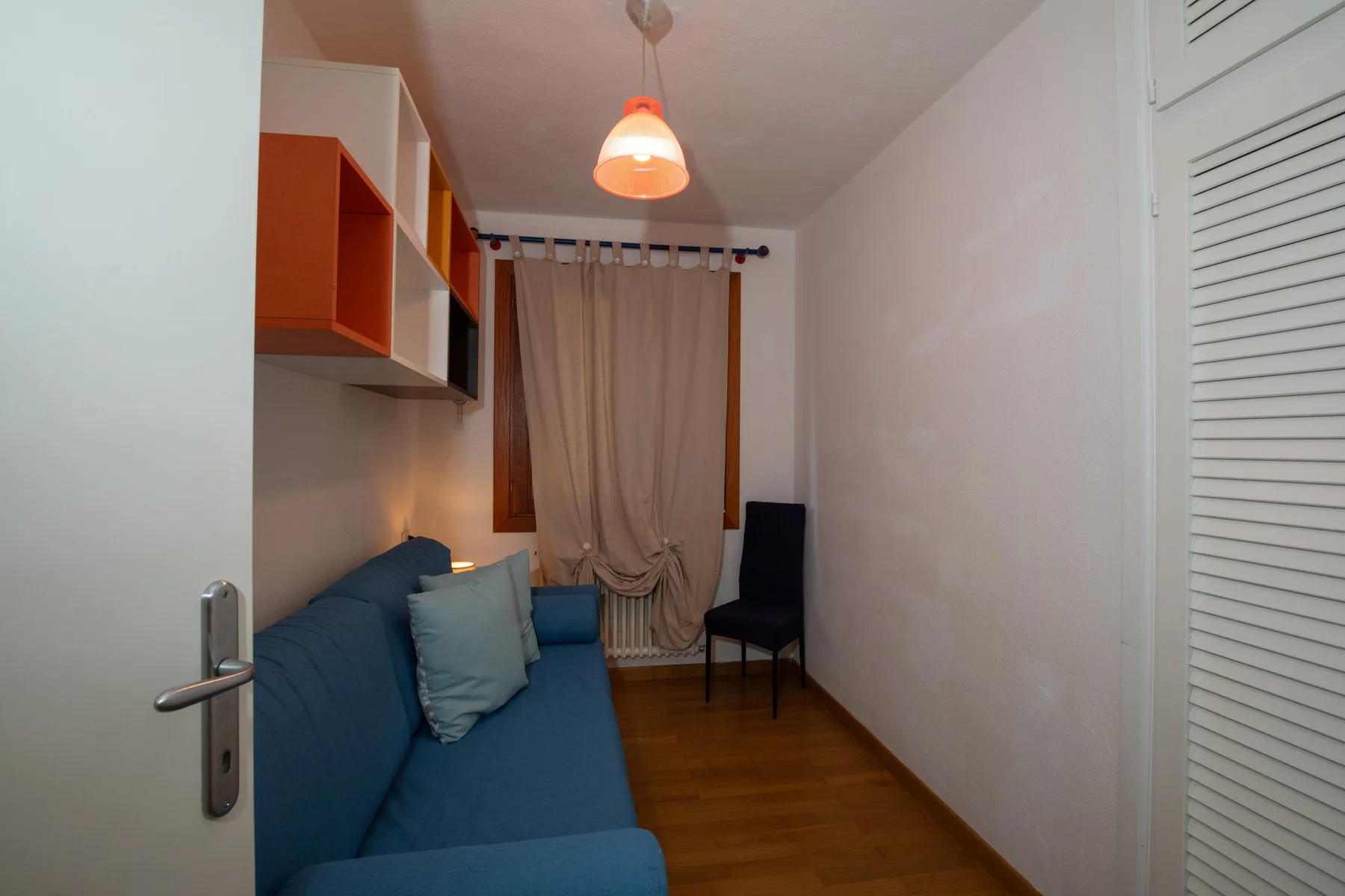 Una habitación estrecha con asientos azules, una ventana con cortinas y armarios de pared.