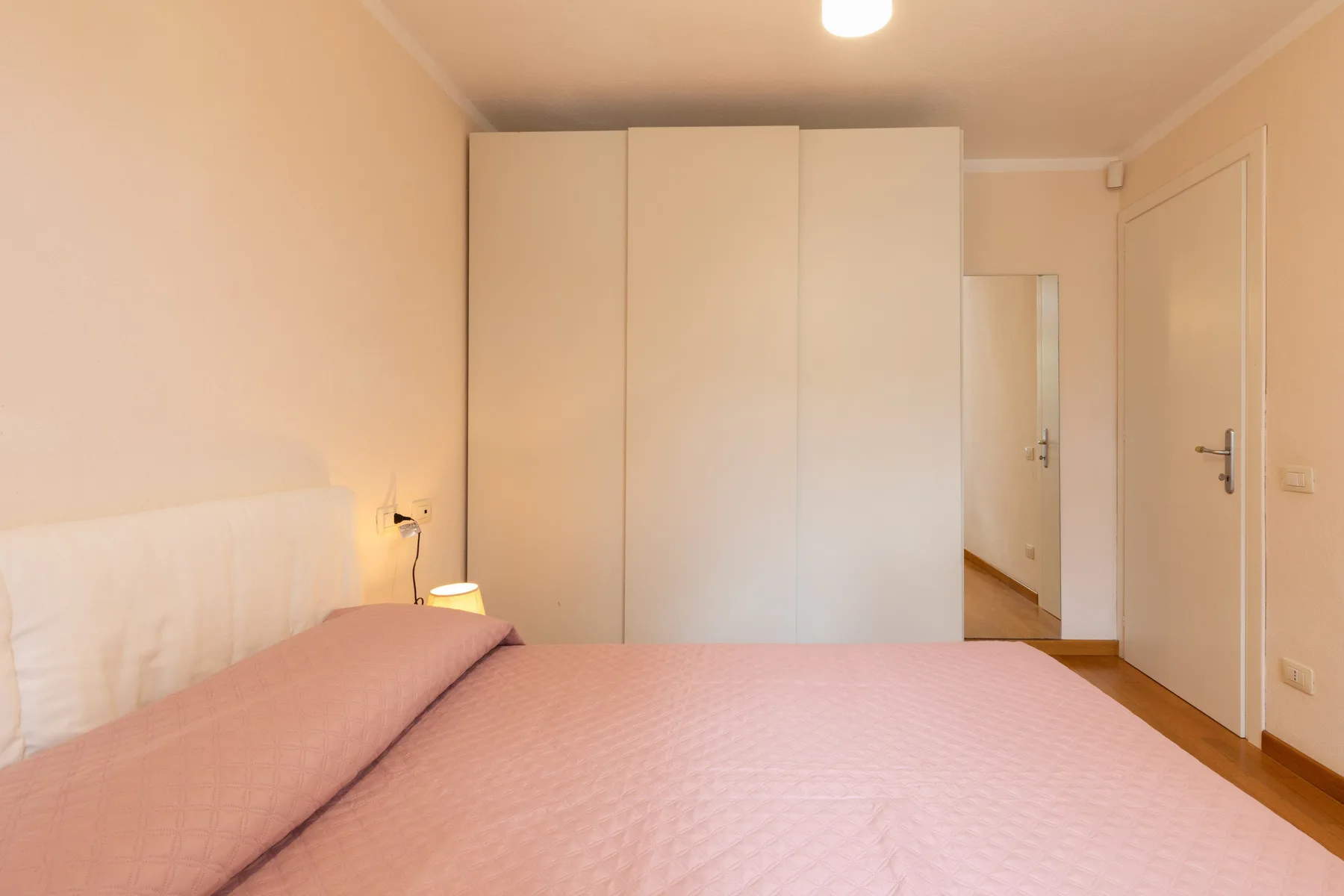 Un dormitorio con una cama rosa y armarios altos blancos.