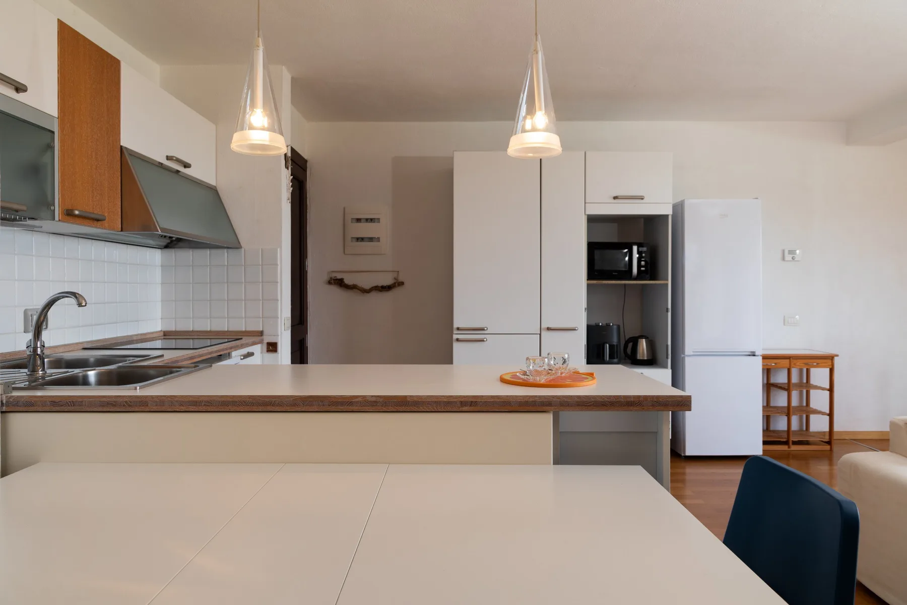 Una cocina luminosa con una barra larga, armarios blancos y lámparas colgantes.